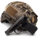 A modern army tactical helmet in camouflage with a Russian police black 9mm pistol. The concept of arming bandits, drug cartels, and insurgents. The photo is isolated on a white background.